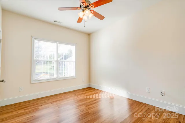 an empty room with wooden floor chandelier fan and windows