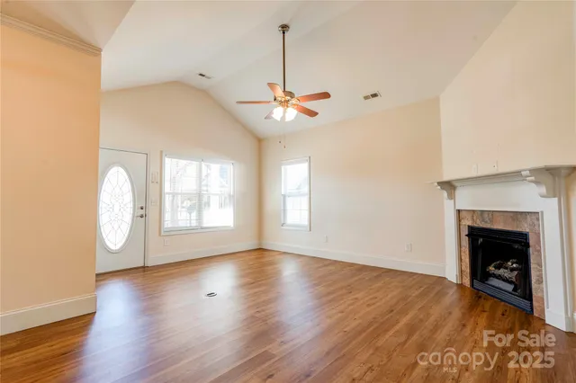 a view of an empty room with wooden floor fireplace and a window