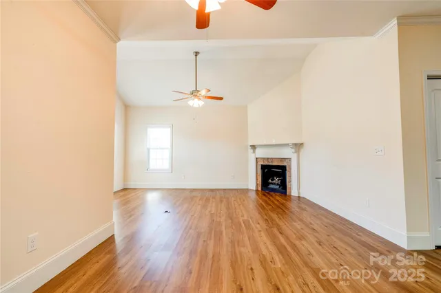 a view of an empty room with wooden floor fireplace and a window