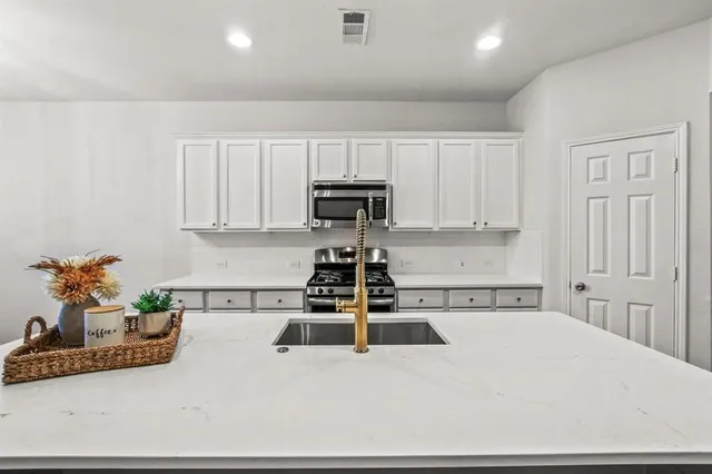 a kitchen with granite countertop a stove a sink dishwasher and white cabinets with wooden floor