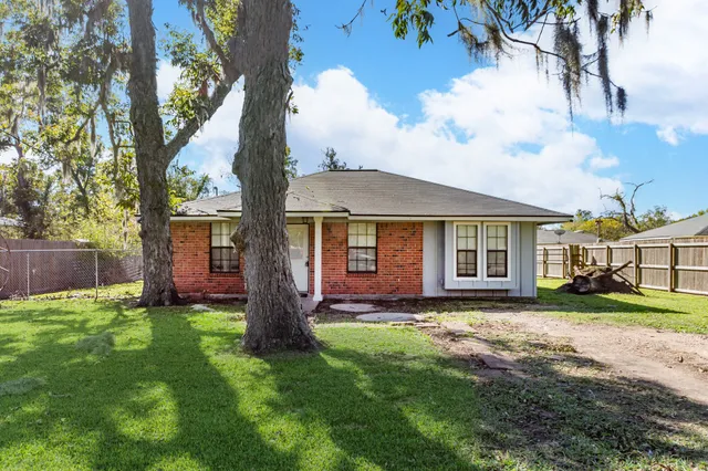 a view of a brick house next to a yard with big trees