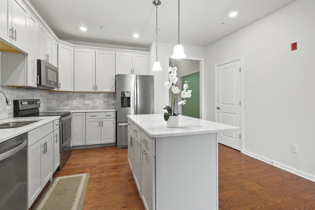 a kitchen with stainless steel appliances granite countertop a sink a stove a refrigerator and island with wooden floor