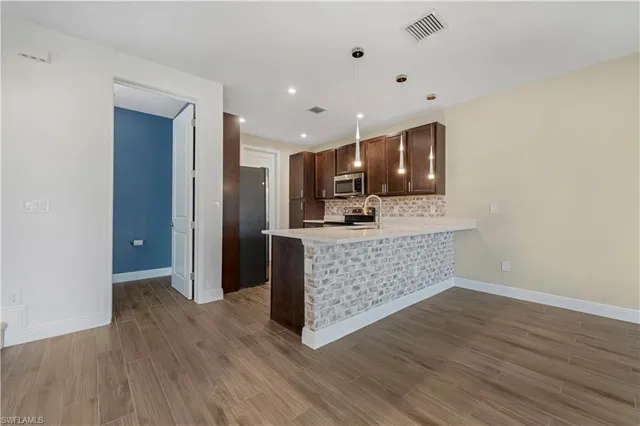 a living room with stainless steel appliances kitchen island wooden floors and fireplace
