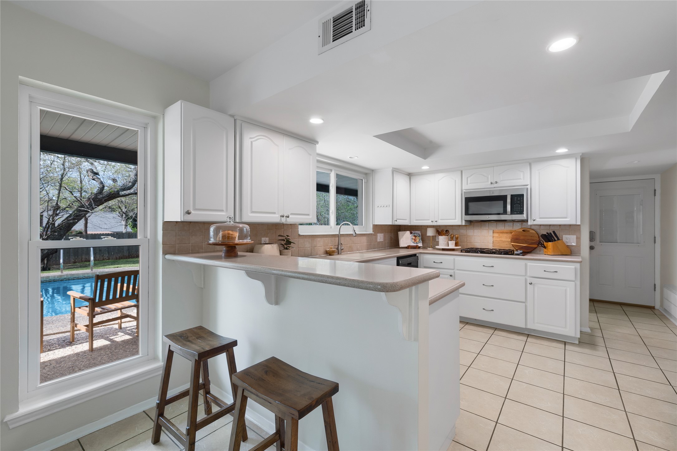 2403 Comburg Castle Way Austin, TX 78748 - Photo 17 of 40 Kitchen featuring white cabinets, light tile patterned floors, a kitchen breakfast bar, backsplash, and a raised ceiling