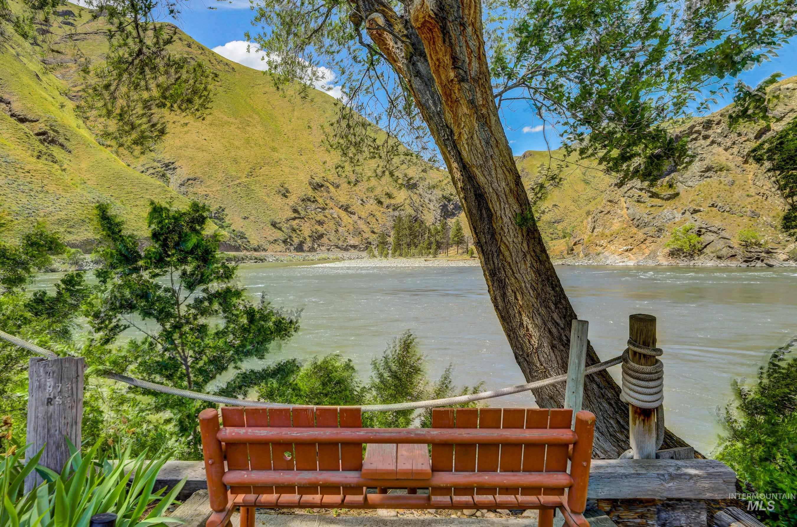 1432 Salmon Drive Riggins, ID 83549 - Photo 3 of 39 Riverfront setting featuring a rustic wooden bench, natural wood railing, mature trees, and mountainous terrain