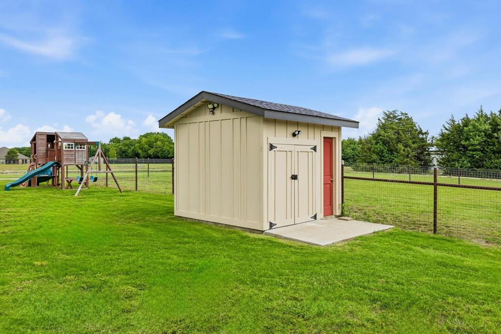 6020 Honeysuckle Road Midlothian, TX 76065 - Photo 31 of 39 Detached utility shed featuring board and batten siding, a gray shingle roof, exterior lighting, and a concrete pad