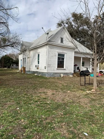 a front view of a house with large trees and lawn chairs