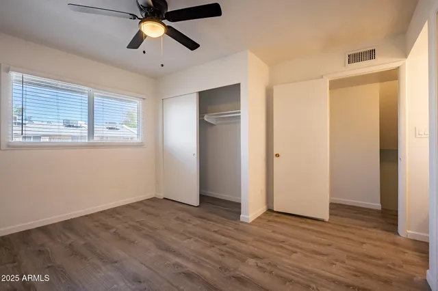 an empty room with wooden floor fan and windows