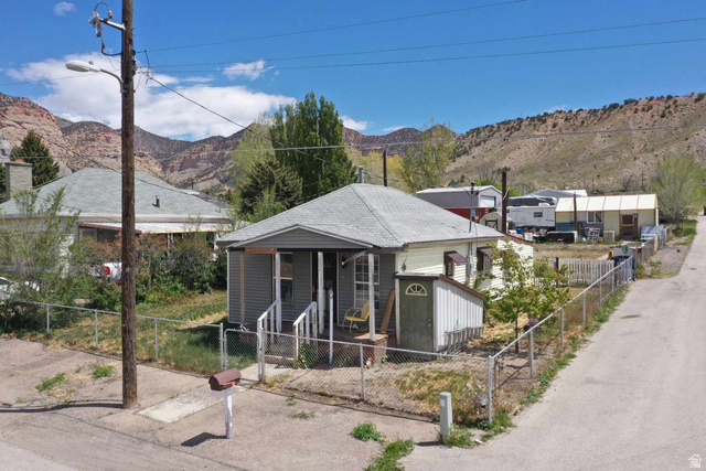 399 2nd E Street Helper, UT 84526 - Photo 13 of 19 Single-story property featuring a front porch with white railings, a detached shed, a chain-link fence, and a gravel driveway