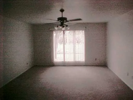an empty room with a chandelier fan and windows