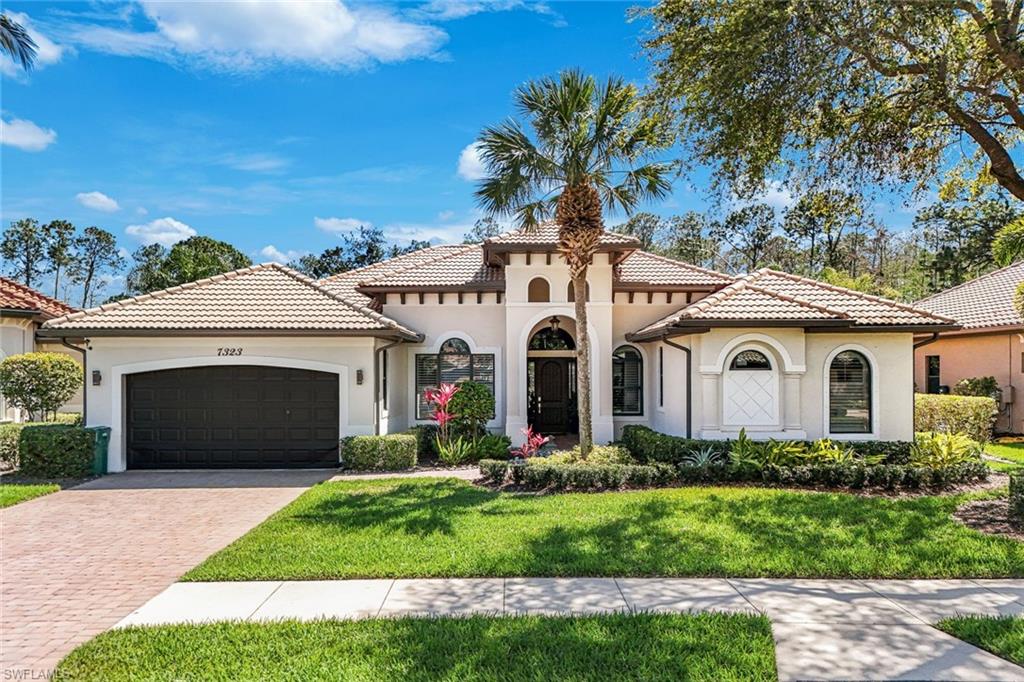 7323 Acorn Way Naples, FL 34119 - Photo 2 of 21 Mediterranean/Contemporary night view featuring stucco siding, garage, decorative driveway, tile roof, and a manicured Lawn.