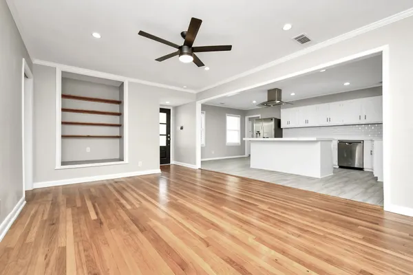 a view of a livingroom with a ceiling fan wooden floor and kitchen view