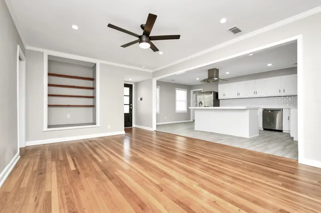 a view of a livingroom with a ceiling fan wooden floor and kitchen view