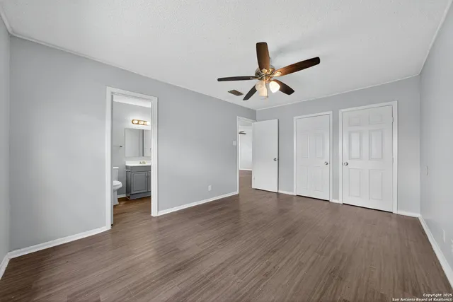 a view of an empty room with wooden floor and a ceiling fan