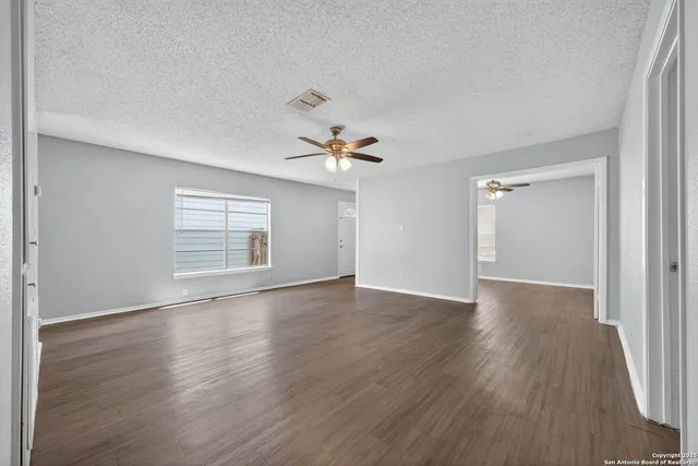 an empty room with wooden floor chandelier fan and windows