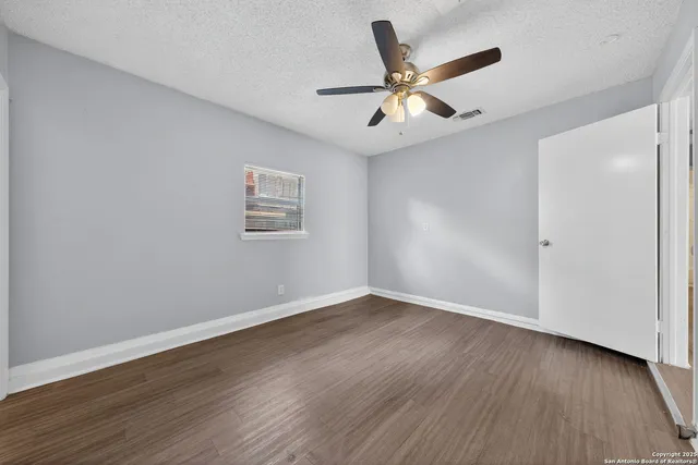 an empty room with wooden floor ceiling fan and windows