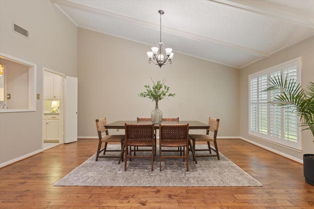 4108 Old Mill Road Waco, TX 76710 - Photo 12 of 39 Elegant dining room showcasing gleaming wood-finish flooring, abundant natural light from shuttered windows, and a pendant light fixture suspended from a coffered ceiling