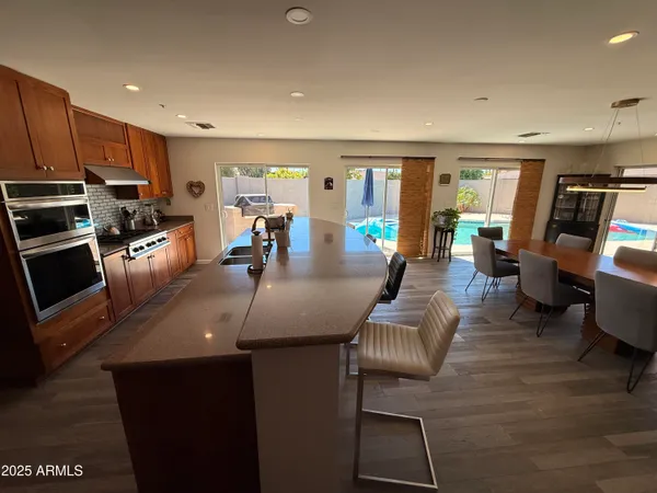 a kitchen with stainless steel appliances granite countertop a stove top oven a sink a dining table and chairs with wooden floor