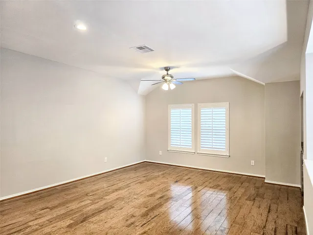 an empty room with wooden floor chandelier fan and windows