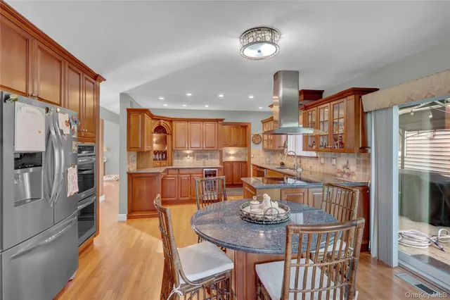 a kitchen with stainless steel appliances kitchen island granite countertop a refrigerator a stove a kitchen island with chairs and wooden floor
