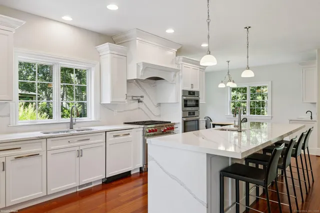 a kitchen with stainless steel appliances granite countertop a stove a refrigerator a kitchen island a dining table and chairs with wooden floor