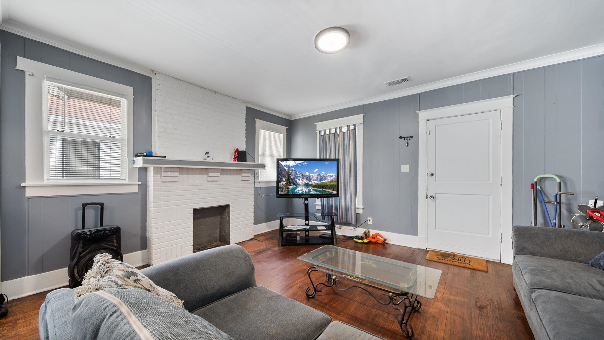 659 Decatur Street Memphis, TN 38107 - Photo 6 of 24 Living area featuring wood-finish flooring, a white-painted brick fireplace with mantel, gray wall paneling, and white trim