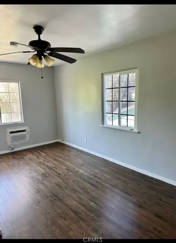 an empty room with wooden floor fan and windows