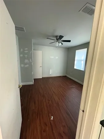 a view of an empty room with wooden floor and a ceiling fan