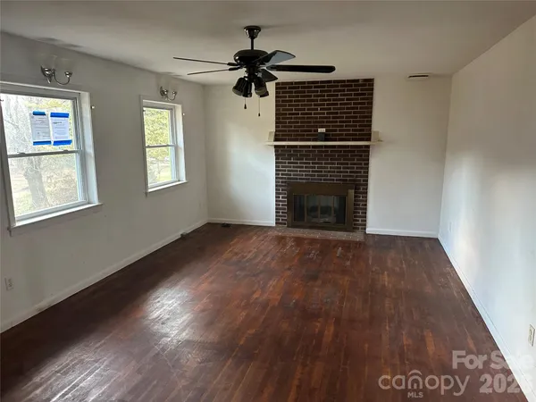 an empty room with wooden floor fireplace and windows