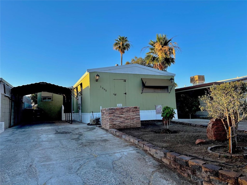 1395 Lause Road Bullhead City, AZ 86442 - Photo 33 of 34 Light green exterior with a covered carport, concrete driveway, and a front yard featuring a low-maintenance landscape design