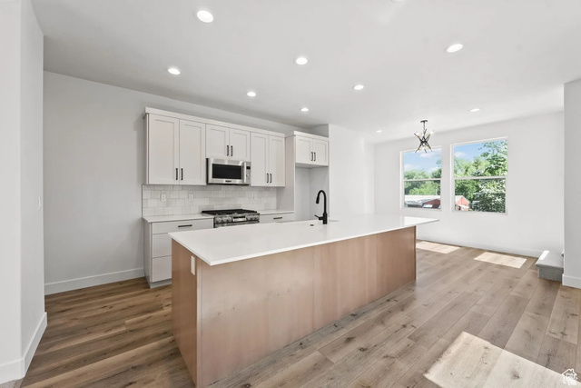 545 East 7215 South Midvale, UT 84047 - Photo 4 of 27 Kitchen with a center island with sink, light wood-style floors, stainless steel appliances, two tone cabinets, and tasteful backsplash