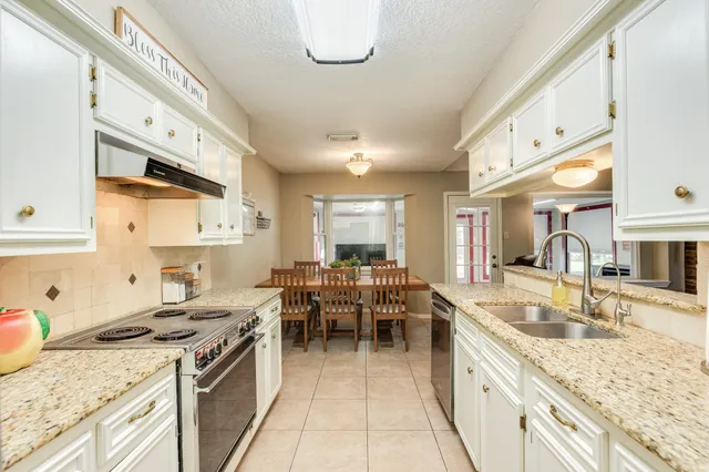 a kitchen with granite countertop a sink a stove top oven a dining table and chairs