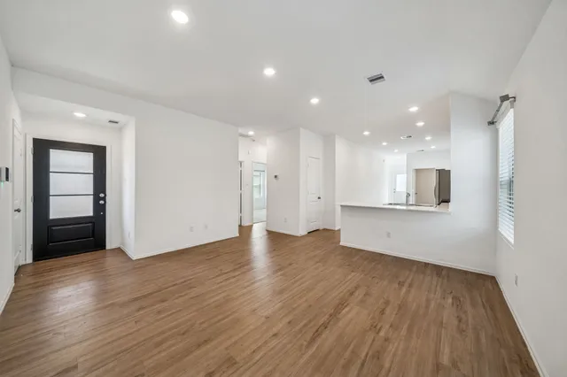 a view of an empty room with wooden floor and kitchen