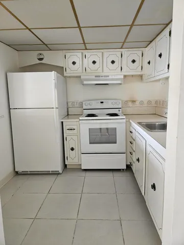 a white kitchen with a refrigerator and white cabinets