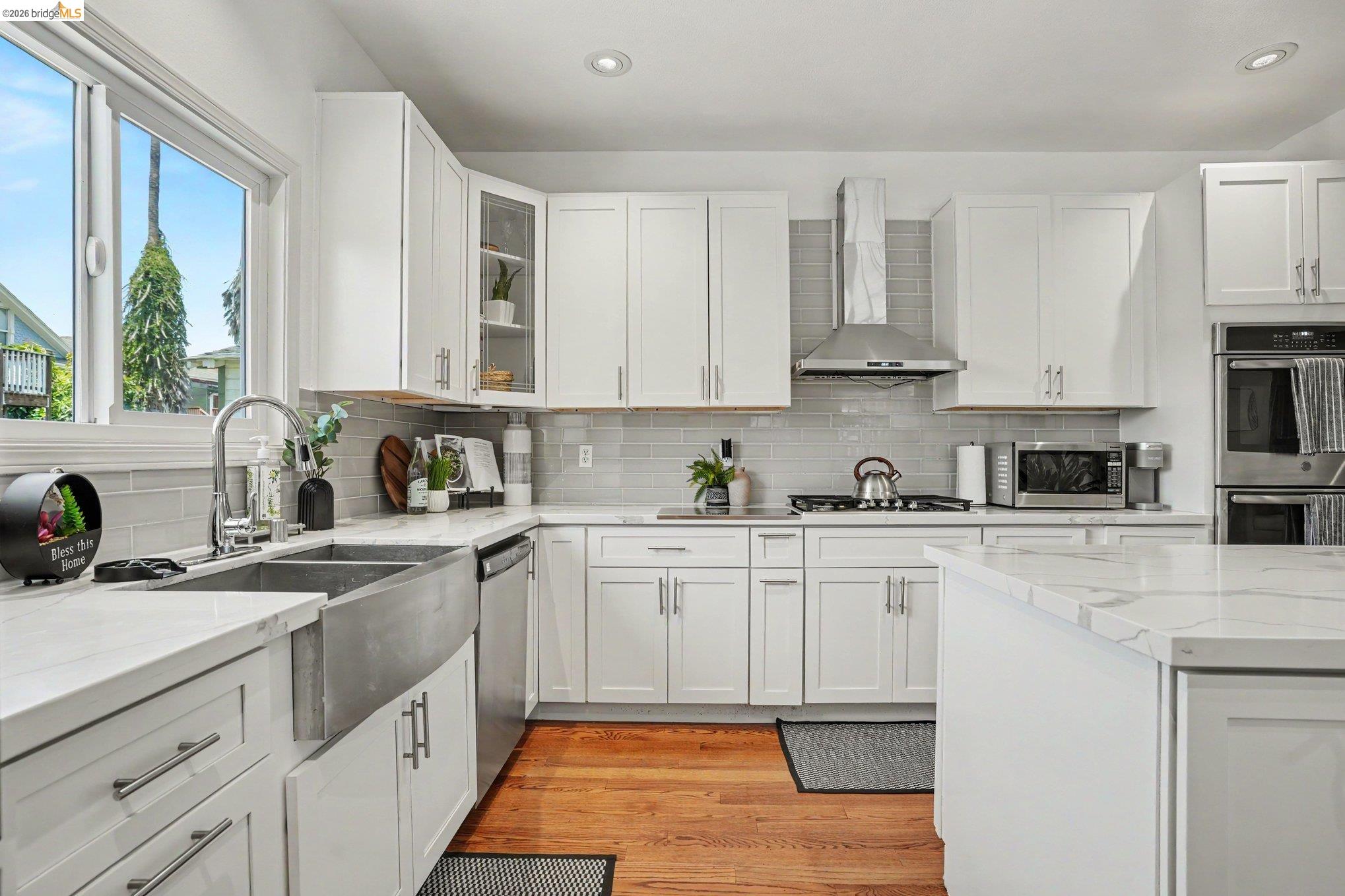 1433 Myrtle Street Oakland, CA 94607 - Photo 7 of 25 Modern kitchen with white shaker cabinetry, stainless steel farmhouse sink, white countertops, stainless steel appliances, and wood-finish flooring