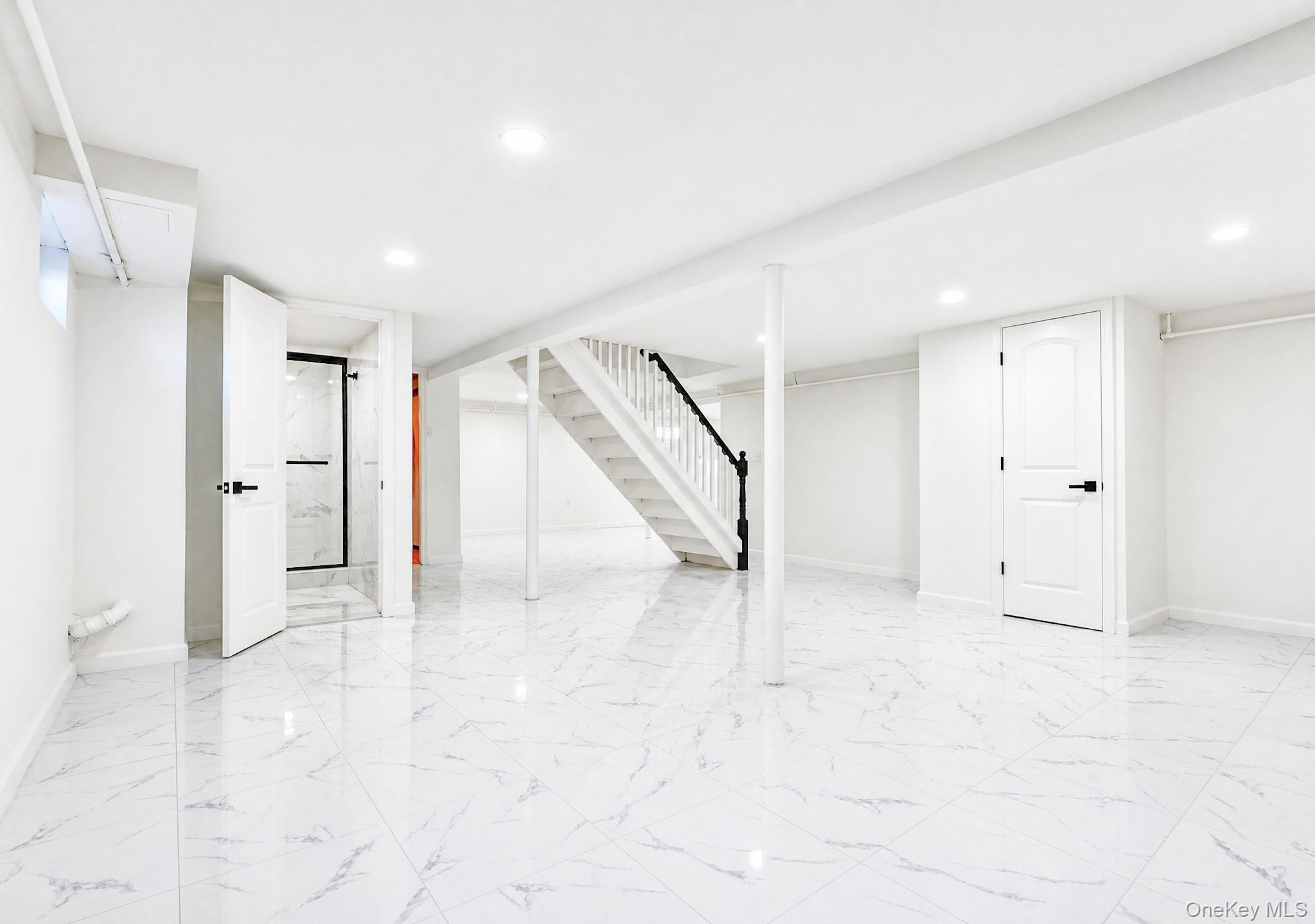 61 Cheshire Road Bethpage, NY 11714 - Photo 21 of 25 Spacious lower-level area featuring white porcelain tile flooring, recessed lighting, and a white painted staircase with a black handrail