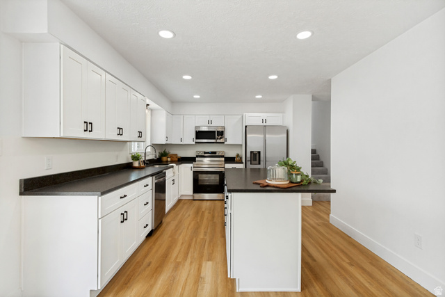 Contemporary kitchen featuring white cabinetry, leathered granite countertops, stainless steel appliances, a center island, and LVP flooring