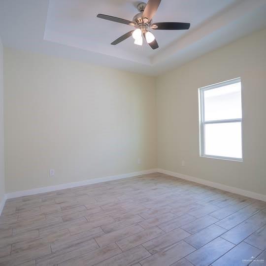 3052 Briggs Road, Unit C Weslaco, TX 78596 - Photo 11 of 16 Room featuring a tray ceiling with a ceiling fan and light fixture, light-toned walls, a single window, and wood-finish tile flooring