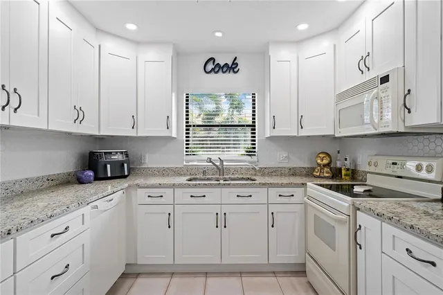 a kitchen with granite countertop white cabinets white appliances and a sink