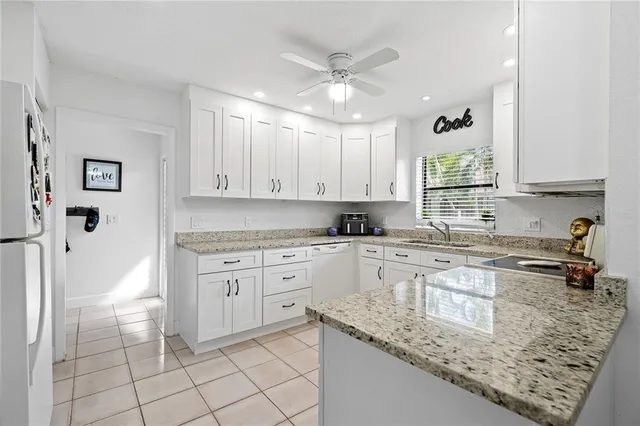 a kitchen with granite countertop white cabinets white appliances with a sink and a counter top space