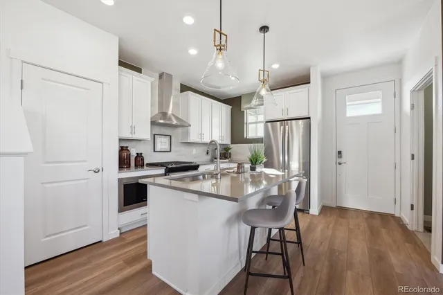 a kitchen with stainless steel appliances granite countertop a refrigerator a sink dishwasher a stove and white countertops with wooden floor