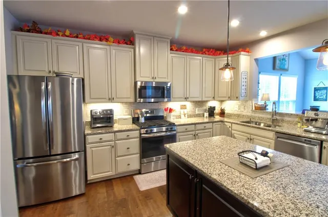 a kitchen with kitchen island granite countertop stainless steel appliances a sink counter top space cabinets and wooden floor