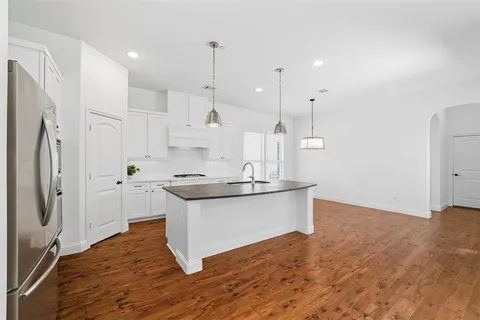 a kitchen with stainless steel appliances granite countertop a sink a stove a refrigerator and white cabinets with wooden floor