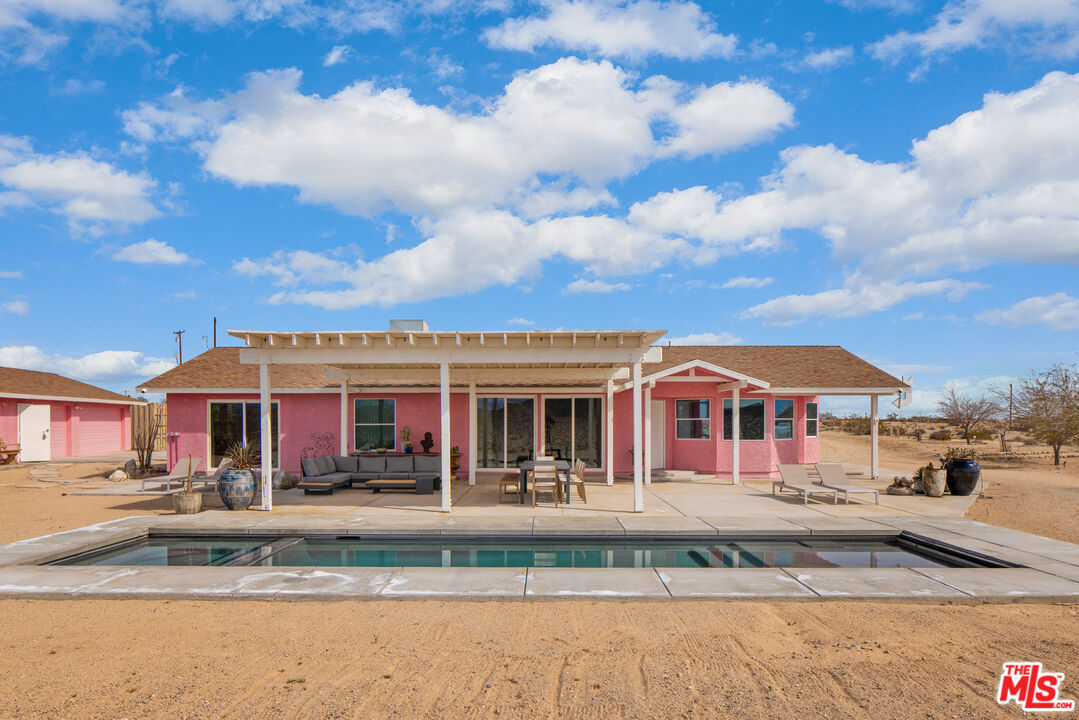 64425 Carot Road Joshua Tree, CA 92252 - Photo 10 of 73 a view of a white house with a large pool with lawn chairs and a small yard