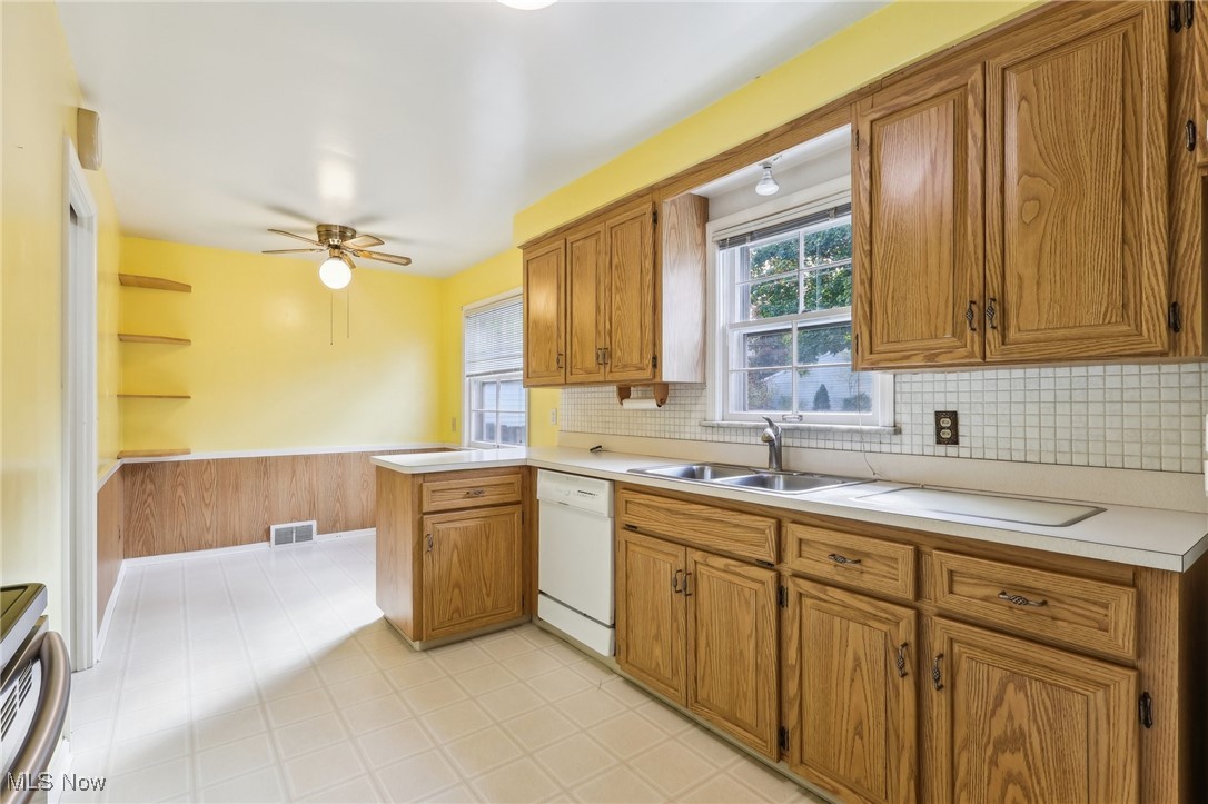 4476 College Road South Euclid, OH 44121 - Photo 9 of 42 Kitchen featuring wooden walls, kitchen peninsula, backsplash, white dishwasher, and sink