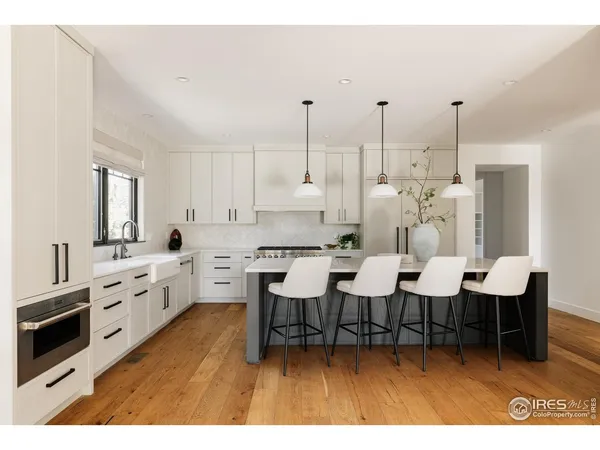 a large white kitchen with stainless steel appliances kitchen island granite countertop a sink dishwasher a stove a dining table with chairs with wooden floor
