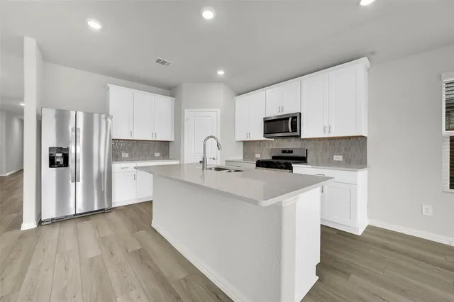 a kitchen with stainless steel appliances a stove a sink a refrigerator white cabinets and wooden floor