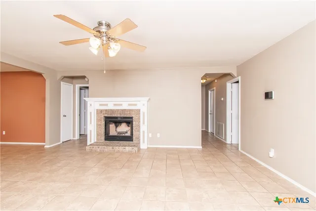 a view of a livingroom with a fireplace a ceiling fan and a kitchen view