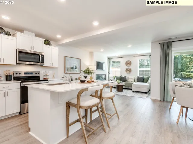 a living room with stainless steel appliances a kitchen island furniture a flat screen tv a rug and a window