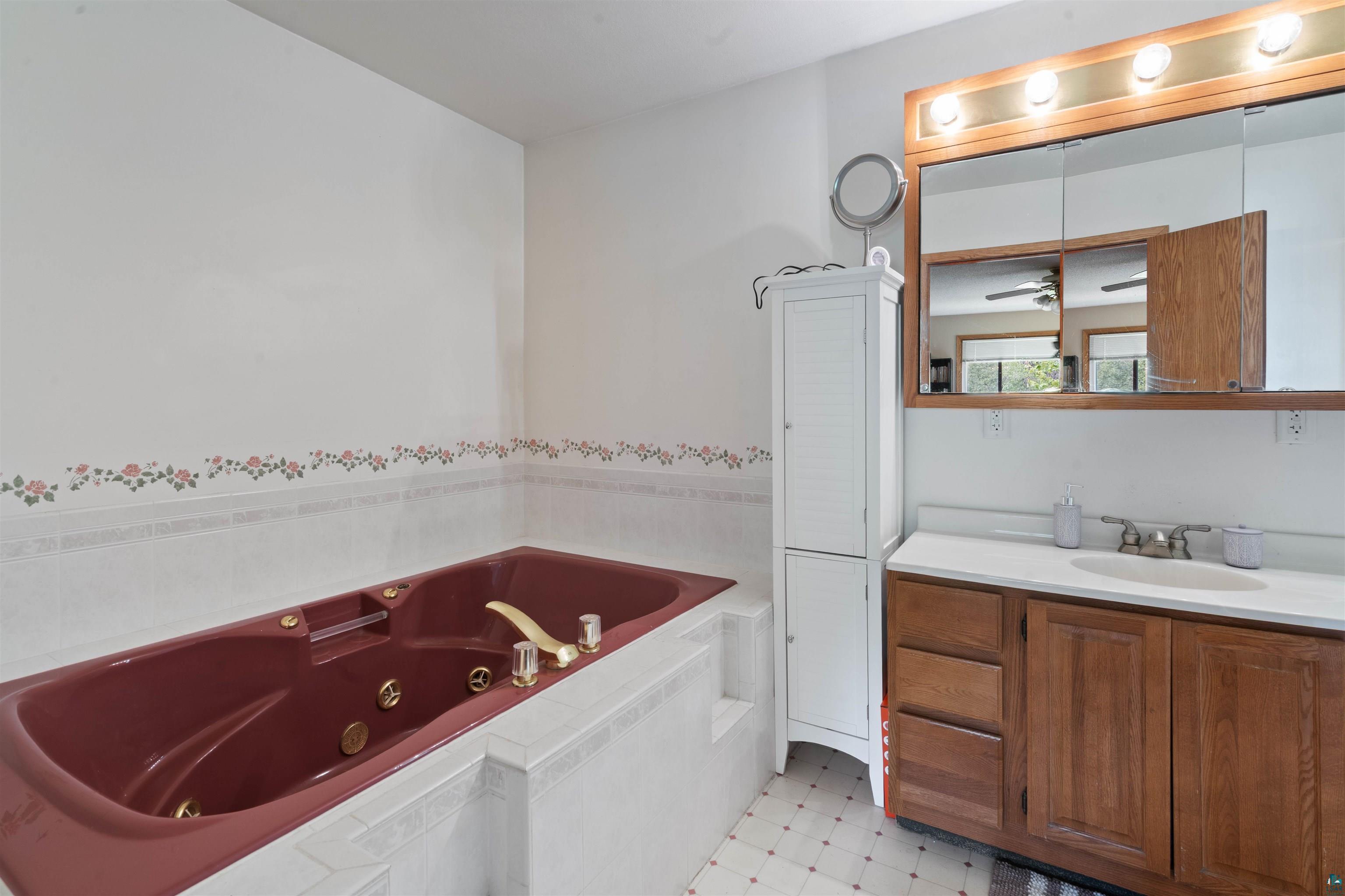 3711 Getchell Road Hermantown, MN 55811 - Photo 13 of 31 Bathroom featuring a burgundy jetted tub, white tiled surround, wood-finish vanity with an integrated sink, and an illuminated medicine cabinet